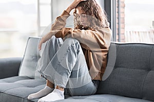 Frustrated European adolescent girl touches head seated on sofa indoor