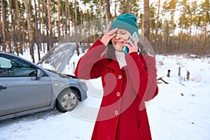 Frustrated female driver in tears of fright talking on mobile phone, calling for roadside assistance, standing on a snowy road in