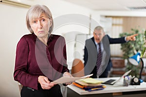 Frustrated female office employee with paper on background of disgruntled manager