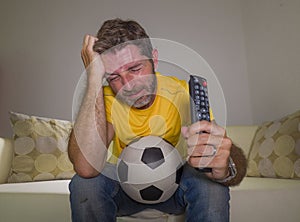 Frustrated football fan in intense emotion - home portrait of young dejected and sad man watching soccer game on television at