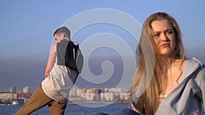 A frustrated girl with anger strikes her hands on the sand on the beach, and the guy does not pay any attention to her