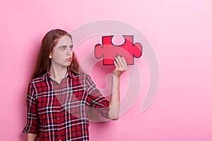 Frustrated girl, holds a puzzle. On a pink background.