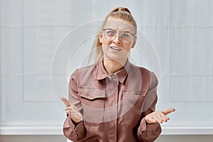 A frustrated girl looks at the web camera and swears. Young woman with glasses.