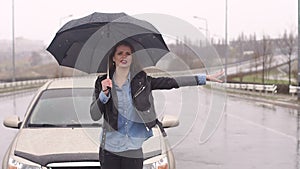 Frustrated girl with an umbrella in the cold rain on the road, she catches a car