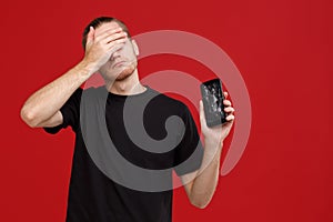 A frustrated guy, holds a broken mobile phone and disappointedly closes his eyes with his hand.