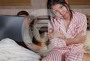 Frustrated Korean woman in bed ignored by workaholic husband or internet social media addict boyfriend networking with laptop in