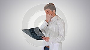 Frustrated male doctor examining computed tomography scan of brain on gradient background.