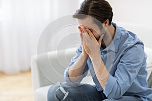 Frustrated Man Crying Covering Face Sitting On Sofa At Home