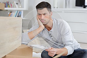 Frustrated man holding instructions for assembling furniture