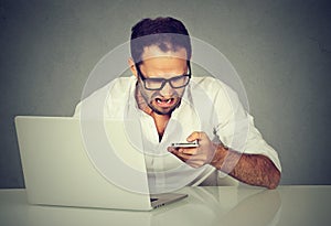 Frustrated man with laptop texting on mobile phone