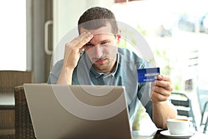 Frustrated man paying with credit card and laptop in a bar