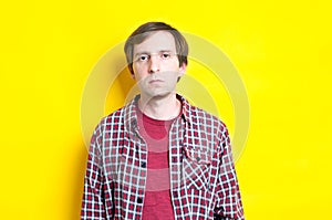 Frustrated man in red checkered shirt looking at camera on yellow background