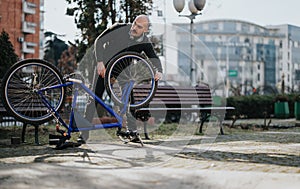 Frustrated man repairing a broken bicycle in an urban park.