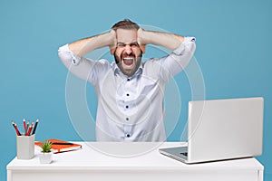 Frustrated man in shirt sit work at desk with pc laptop isolated on blue background. Achievement business career