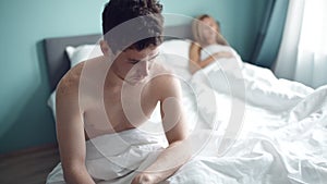 Frustrated man sitting on bed on different side of woman. Young unhappy couple having problem in bedroom, quarrel