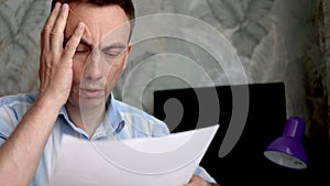 Frustrated man sitting at desk with paper bills. Bankruptcy concept