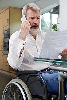 Frustrated Man In Wheelchair Making Phone Call Whilst Reading Le