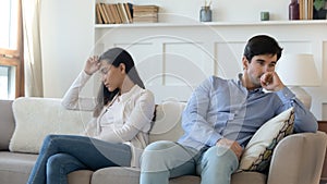 Frustrated married couple sitting separate on couch after family conflict