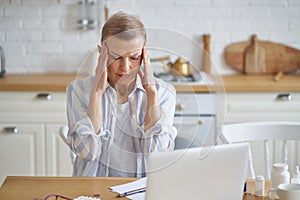 Frustrated mature woman suffering from headache while working online from home