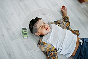 Frustrated Moody tween boy lying on floor with car toy at home