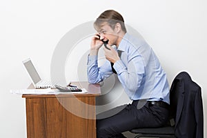 Frustrated office worker on the phone. chews tie