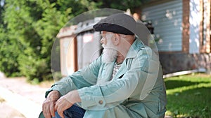 Frustrated old Caucasian man sitting on road curb looking around in slow motion. Homeless senior retiree with gray hair