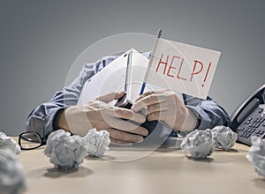 Frustrated and overworked businessman burying his head under a laptop computer asking for help