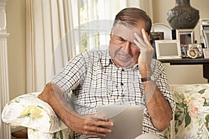 Frustrated Retired Senior Man Sitting On Sofa At Home Using Digital Tablet