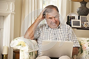 Frustrated Retired Senior Man Sitting On Sofa At Home Using Laptop