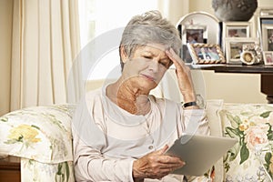 Frustrated Retired Senior Woman Sitting On Sofa At Home Using Digital Tablet