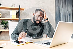 Frustrated sad black guy is watching at laptop screen