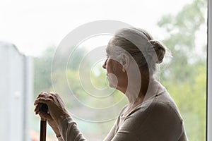 Frustrated sad lonely elderly woman sitting by window glass