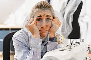 frustrated seamstress with hands on chin in the workshop studio for sewing machine. Workplace of seamstress