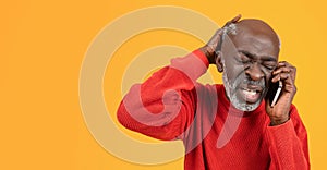 Frustrated senior black man in a red sweater and hat feeling stressed while talking on the phone