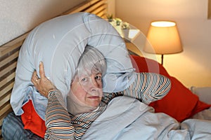 Frustrated senior woman covering ears with pillow