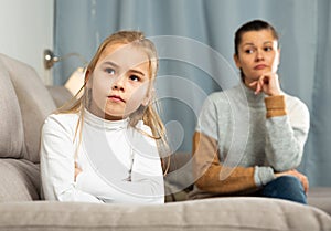 Frustrated small girl sitting at sofa, having conflict with mother