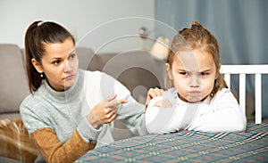 Frustrated small girl sitting at sofa, having conflict with mother