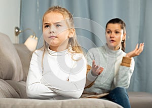 Frustrated small girl sitting at sofa, having conflict with mother