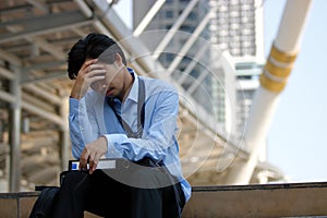 Frustrated stressed Asian businessman with hand on forehead sitting on staircase in the city. Depressed unemployment business conc