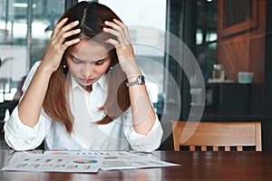 Frustrated stressed young Asian business woman analyzing paper work or charts in workplace. Thinking and thoughtful concept.