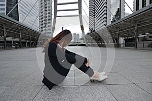 Frustrated stressed young Asian business woman sitting and hugging his knees up to the chest on the floor at urban city background
