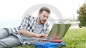 Frustrated student e learning with a laptop on the grass