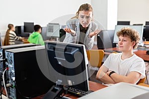 Frustrated teacher talking to neglectful teenage student in computer class