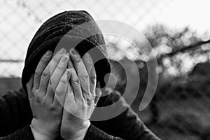 Frustrated teenage boy covering hes face in front of correctional institutes wired fence, conceptual image of juvenile delinquency photo