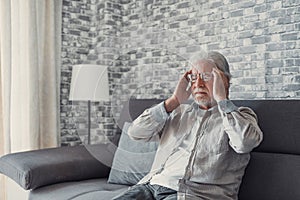 Frustrated unhealthy senior mature man touching head, having painful feelings sitting alone at home. Unhappy middle aged retired