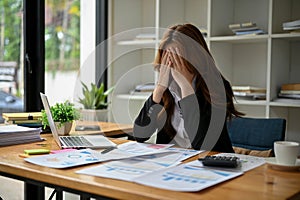 A frustrated and upset Asian businesswoman covering her face with her hands, crying at her desk