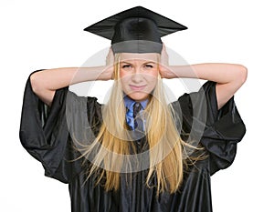 Frustrated woman in graduation gown closing ears