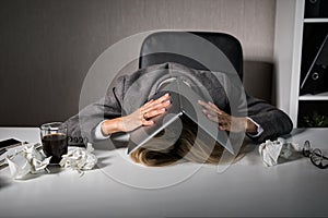 Frustrated woman hiding under laptop in office