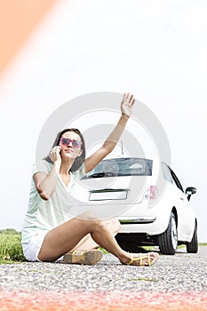 Frustrated woman hitchhiking while using cell phone by broken down car