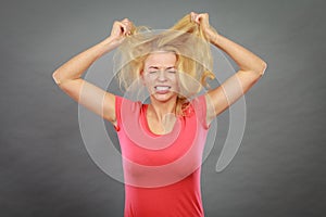 Frustrated woman holding her damaged blonde hair